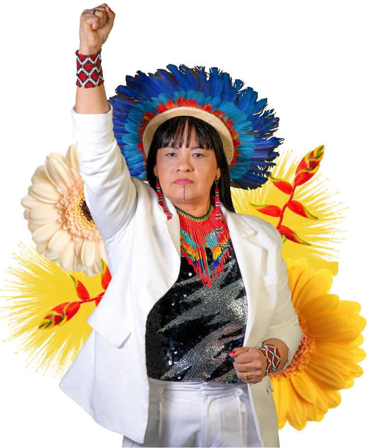Luciene Kayabi de punho erguido, com cocar azul e flores ao fundo